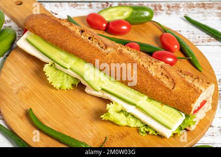 Baguette-Sandwich. Sandwich mit Oliven, Salat, Tomaten, Gurken, Cheddar und Fetakäse auf Holzhintergrund Stockfoto