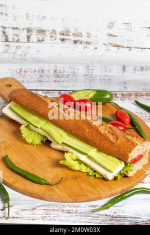 Baguette-Sandwich. Sandwich mit Oliven, Salat, Tomaten, Gurken, Cheddar und Fetakäse auf Holzhintergrund Stockfoto