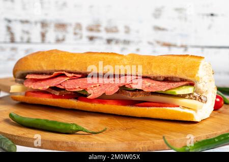 Baguette-Sandwich. Sandwich mit Salami, Roastbeef, Cheddar, Tomaten und Gurke auf Holzhintergrund Stockfoto