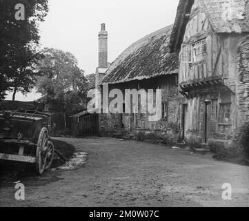 Ein englisches Schwarz-Weiß-Foto aus dem späten 19.. Jahrhundert, das traditionelle Backsteinhäuser mit Strohdächern in einem Dorf mit einem Pferdewagen vor der Tür zeigt. Stockfoto