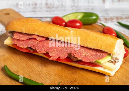 Baguette-Sandwich. Sandwich mit Salami, Roastbeef, Cheddar, Tomaten und Gurke auf Holzhintergrund Stockfoto