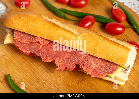 Baguette-Sandwich. Sandwich mit Salami, Roastbeef, Cheddar, Tomaten und Gurke auf Holzhintergrund Stockfoto