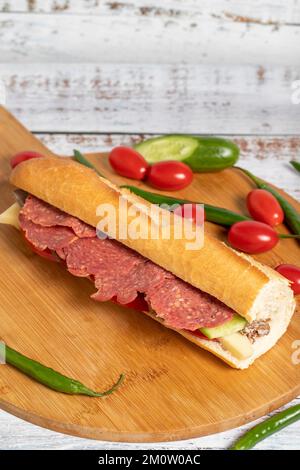 Baguette-Sandwich. Sandwich mit Salami, Roastbeef, Cheddar, Tomaten und Gurke auf Holzhintergrund Stockfoto