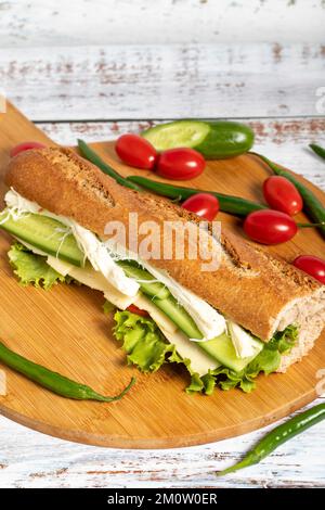 Baguette-Sandwich. Sandwich mit Oliven, Salat, Tomaten, Gurken, Cheddar und Streichkäse auf Holzhintergrund Stockfoto