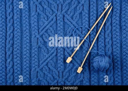 Ball of thread and knitting needles lie on a blue knitted fabric. The concept of spending time at home and knitting warm clothes for winter and autumn Stockfoto