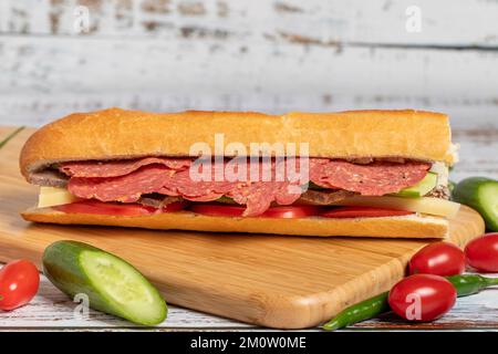 Baguette-Sandwich. Sandwich mit Salami, Roastbeef, Cheddar, Tomaten und Gurke auf Holzhintergrund Stockfoto