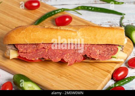 Baguette-Sandwich. Sandwich mit Salami, Roastbeef, Cheddar, Tomaten und Gurke auf Holzhintergrund Stockfoto