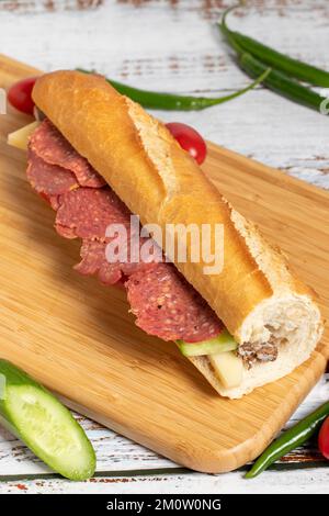 Baguette-Sandwich. Sandwich mit Salami, Roastbeef, Cheddar, Tomaten und Gurke auf Holzhintergrund Stockfoto