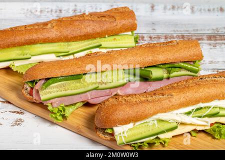 Verschiedene köstliche Baguette-Brotsandwiches auf dem Schneidebrett. Salami, geräuchertes Fleisch, Oliven, Salat, Tomaten- und Gurken-Sandwich Stockfoto