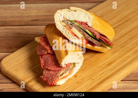 Baguette-Sandwich. Sandwich mit Salami, Roastbeef, Cheddar, Tomaten und Gurke auf Holzhintergrund Stockfoto