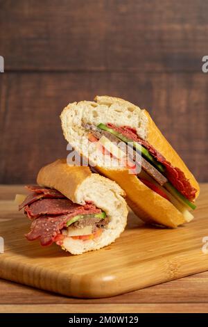 Baguette-Sandwich. Sandwich mit Salami, Roastbeef, Cheddar, Tomaten und Gurke auf Holzhintergrund Stockfoto