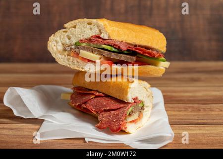 Baguette-Sandwich. Sandwich mit Salami, Roastbeef, Cheddar, Tomaten und Gurke auf Holzhintergrund Stockfoto