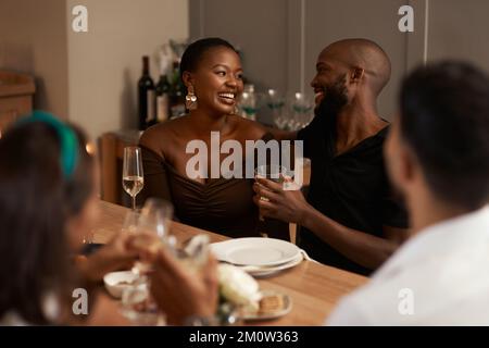 Schwarzes Paar, Champagner und Partyfeier mit Freunden zum Neujahr, Weihnachtsessen oder Festessen im Haus. Mann und Frau, die reden und Stockfoto