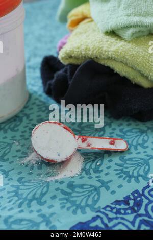 Waschpulver in Plastiklöffel auf blauem Hintergrund Stockfoto