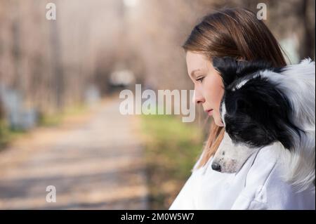 Eine weiße Frau, die im Herbstpark Border Collie umarmt. Porträt eines Mädchens mit Hund. Stockfoto