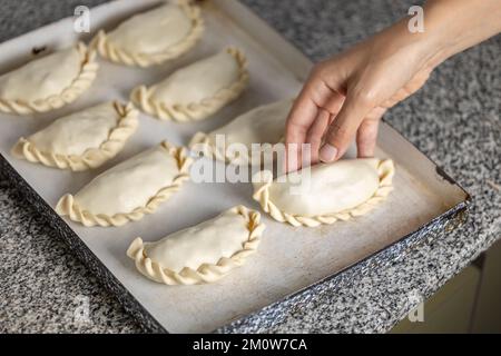 Frauenhände, die argentinische Empanadas auf einen Teller legen. Stockfoto