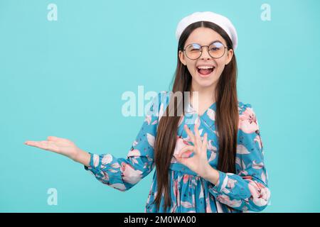 Positive Teenager Kind zeigt sich mit fröhlichem Ausdruck beiseite, zeigt erstaunlich auf leeren leeren Raum. Werbung und Mockup. Glücklicher Teenager, positiv Stockfoto