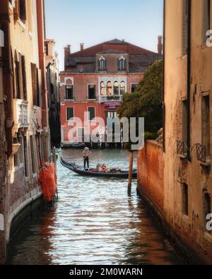 Ein flüchtiger Blick auf eine Gondel, die sich langsam entlang des Canal Grande bewegt, vorbei an einem der vielen Seitenkanäle im historischen Venedig, Italien. Stockfoto