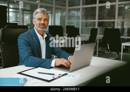 Vielbeschäftigter, reifer Geschäftsmann, der im modernen Coworking sitzt und am Laptop arbeitet Stockfoto