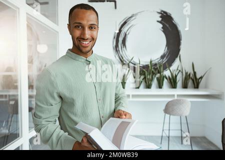 Lächelnder afrikanischer Geschäftsmann, der im modernen Büro steht und Buch hält Stockfoto