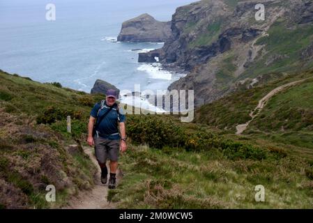 Ein Mann, der auf einem Fußweg am Samphire Rock, Northern Door Arch und Cambeak vom South West Coastal Path in Cornwall, England, Großbritannien, spaziert. Stockfoto