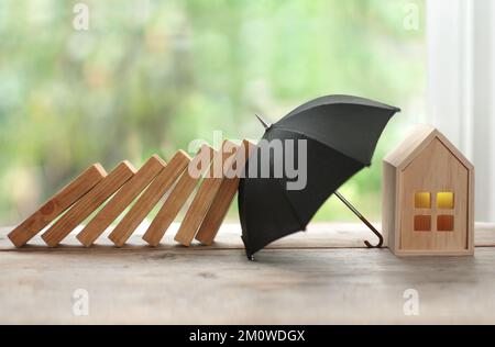 Regenschirm schützt Haus vor Dominoeinsturz, Versicherungskonzept Stockfoto