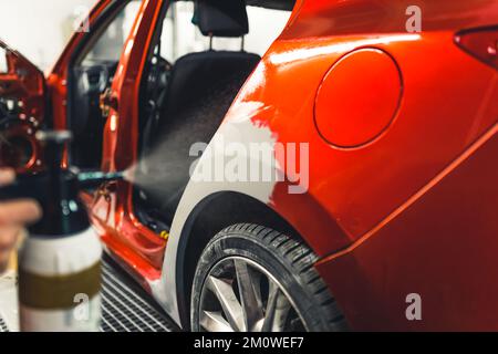 Fahrzeugkonzept für die Nachbearbeitung. Innenaufnahme einer unbekannten Person mit Autolack auf rotem Auto. Facharztarbeit bei Mechanikern. Hochwertiges Foto Stockfoto