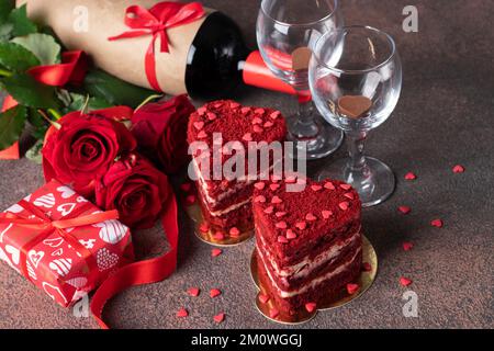 Kuchen Roter Samt in Form von Herzen, Rosen und Flaschenwein zum Valentinstag auf braunem Hintergrund, Close Up Stockfoto