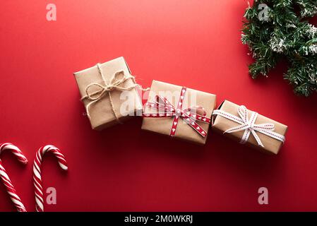 Weihnachtsgeschenke verpackt aus Kraftpapier dekorierte Schleife und Tannenzweige auf marsala-rotem Hintergrund. Flach liegend, Draufsicht. Weihnachten, Winter Stockfoto