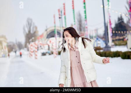 Die stilvolle, glückliche junge Frau läuft draußen auf der Eisbahn. Festliche Feiertagsstimmung. Träume werden wahr Konzept. Stockfoto