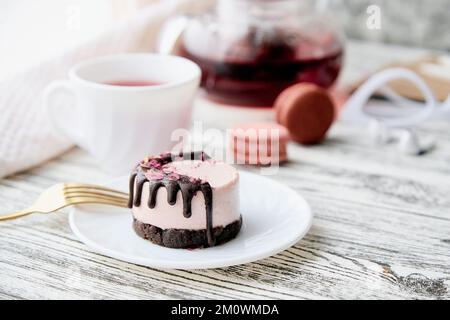 Weibliches Frühstück - rosafarbener Himbeerkuchen ohne Backwaren und eine Tasse Tee. Gesundes veganes Dessert. Romantisches Abendessen mit Kerzen. Stockfoto