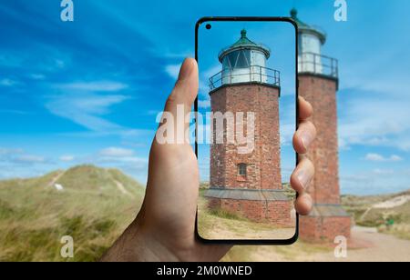 Ein Tourist fotografiert mit einem Handy den Leuchtturm „rotes kliff“ auf der Insel Sylt. Stockfoto