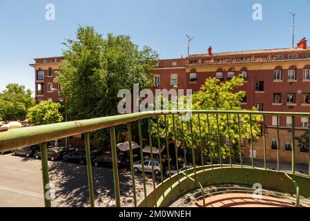 Blick auf ein Gebäude mit grünen Bäumen an der Fassade von einer Terrasse mit grünem Metallgeländer Stockfoto