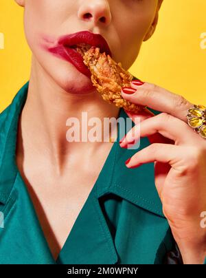 Zugeschnittenes Bild einer Frau in grünem Mantel mit rotem Lippenstift, die gebratenes Hähnchen isst, Nuggets auf gelbem Hintergrund. Fastfood. Essen Pop Art Stockfoto