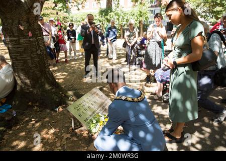 Der Bürgermeister von Camden, Cllr Nasim Ali, legt in der Nähe des Kirschbaums, der zum Gedenken an die Opfer von Hiroshima während eines Ereignisses in London gepflanzt wurde, Blumengewächse ab. Stockfoto