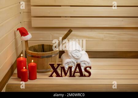 Sauna. Holzeimer, brennende Kerzen, Handtücher und weihnachtsmannmütze, Xmas-Inschrift Stockfoto