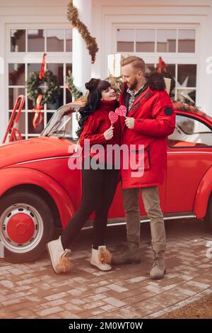 Süßes Paar in passenden Outfits, das neben dem roten Auto posiert Stockfoto