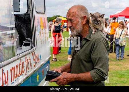 A man kauft ein Eis mit Einer Hauskatze auf den Schultern, Hartfield Village Fete, Hartfield, East Sussex, Großbritannien. Stockfoto