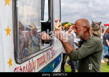 A man kauft ein Eis mit Einer Hauskatze auf den Schultern, Hartfield Village Fete, Hartfield, East Sussex, Großbritannien. Stockfoto