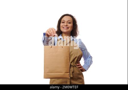 Konzentrieren Sie sich auf eine Einweg-Papiertüte mit frisch gelieferten Speisen und Getränken in den Händen einer lächelnden Kellnerin in beigefarbener Schürze Stockfoto