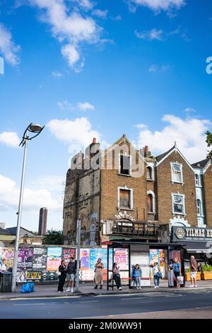 Peckham Rye in Süd-London, England, Großbritannien, mit ausgebranntem Gebäude und Menschen, die unter blauem Himmel an der Bushaltestelle warten Stockfoto