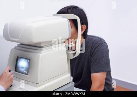 Junger, gutaussehender Asiate macht eine Augenuntersuchung mit einem optischen Augen-Testgerät Stockfoto