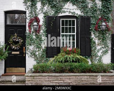 Vorderseite des alten Backsteinhauses mit Weihnachtskranz an der Eingangstür und Heidelbeerdekorationen Stockfoto