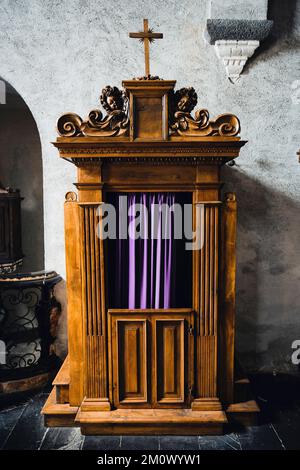 Typische alte hölzerne Beichtkabine an einer Kirche, mit blauen Vorhängen. Stockfoto