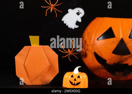 Orangefarbene Kürbisse, ein Geist, Spinnen und Spinnennetze auf schwarzem Hintergrund, eine Halloween-Feier. Stockfoto