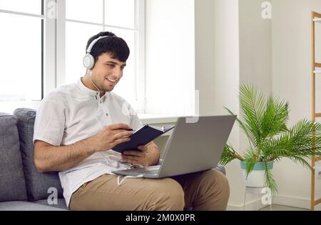 Glücklicher junger Mann, der seinen Laptop-Computer benutzt, um an Online-Kursen in Fremdsprache teilzunehmen Stockfoto