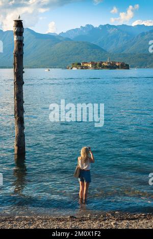 Weiblicher Urlaub, Rückblick im Sommer einer jungen Frau, die im Lago Maggiore stand und ein Foto von Isola dei Pescatori, Piemont, Italien machte Stockfoto