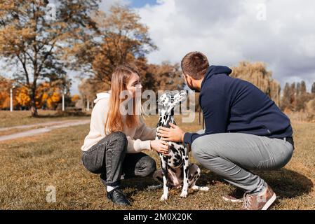 Ein junges Paar amüsiert sich draußen mit einem dalmatinischen Hund. Stockfoto