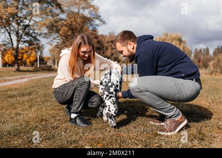 Ein junges Paar amüsiert sich draußen mit einem dalmatinischen Hund. Stockfoto