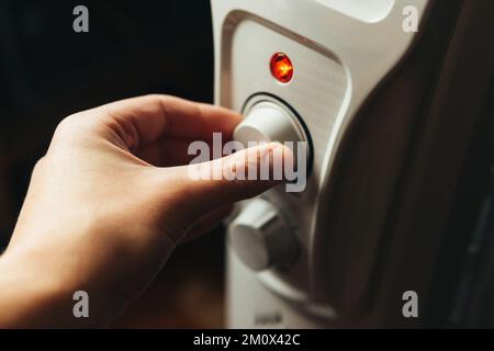 Mann, der zu Hause die elektrische Ölheizung anstellt. Kalter Winter, Wirtschaftskrisenkonzept. Stockfoto